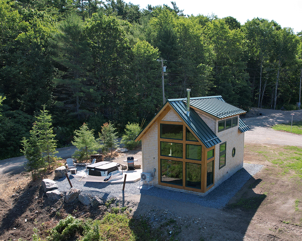 Wood shingle siding on a newly constructed cabin with large windows and a hot tub surrounded by the Maine woods.