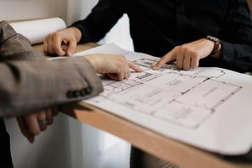 Two sets of hands pointing at a architectural design plan.