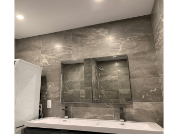 Bathroom vanity with mirrors, gray marble walls, and double sink.
