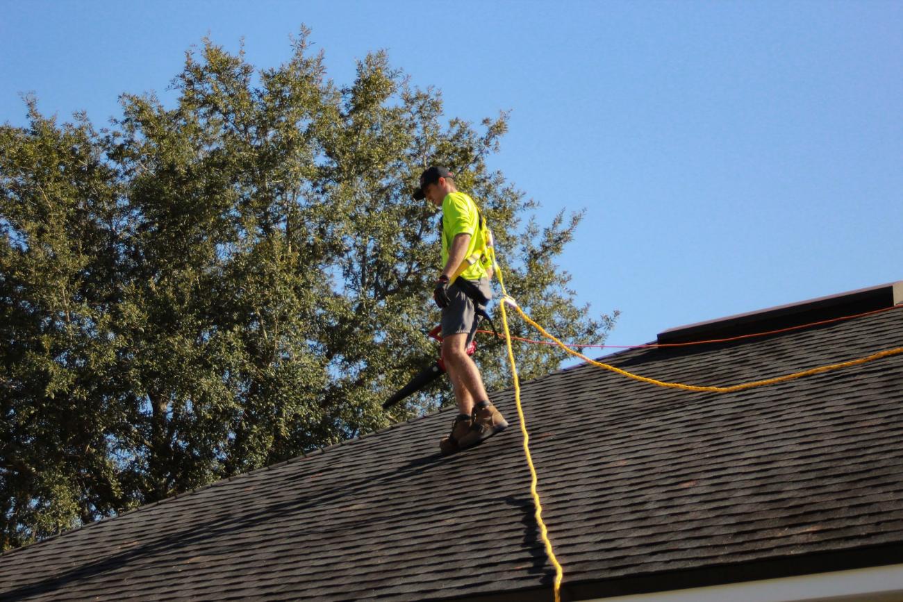 Roofer on a slant shingle roof wearing a safety line.