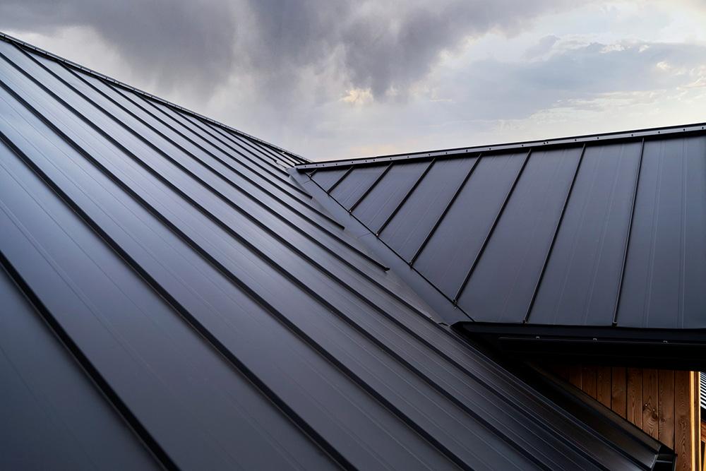 Black Metal roofing against cloudy sky. The roof lines converge at a seamless angle.