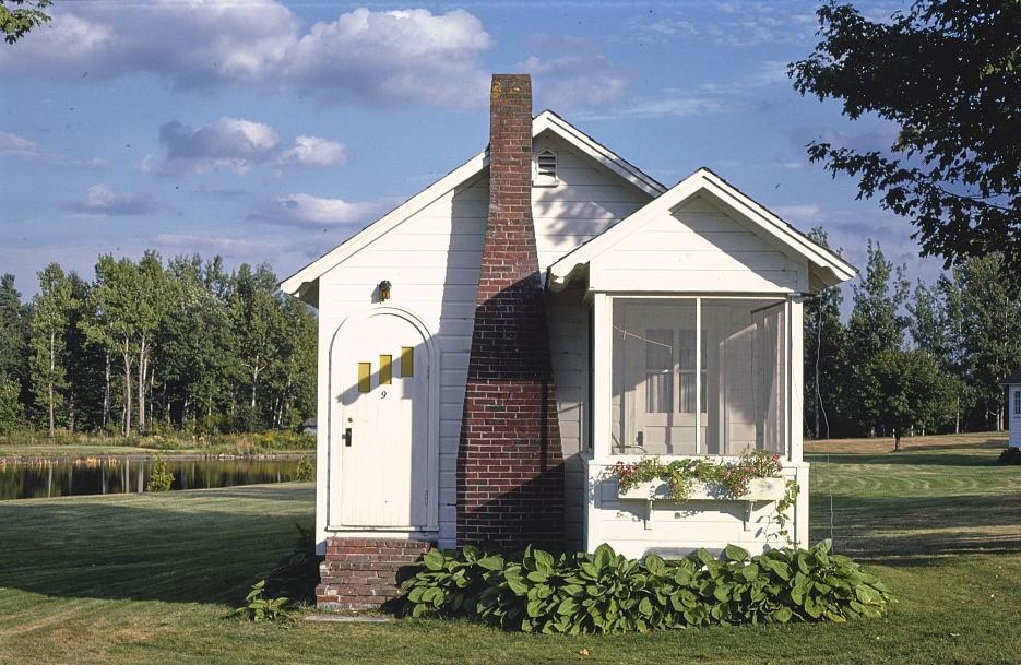 A single story cabin with brick chimney and small porch on clear day.