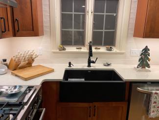 Black stone apron sink with new wooden cabinets and white countertops.