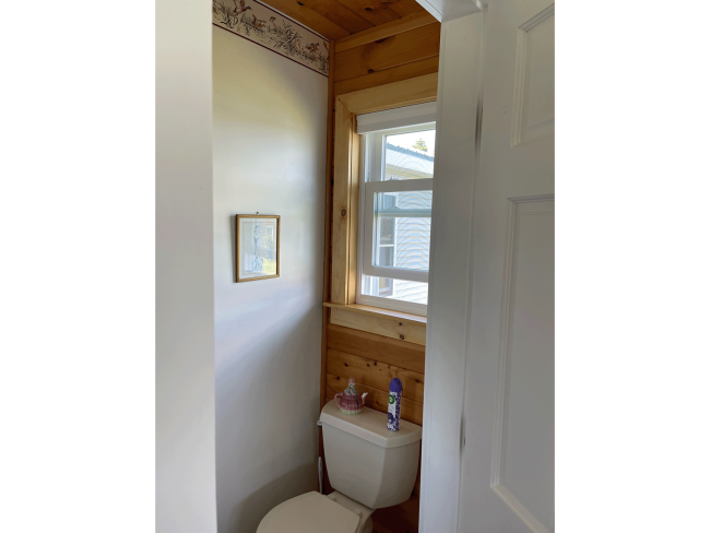 Wood trim surrounds a window above a bathroom toilet.