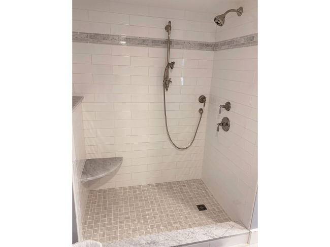 An alternative view of the walk in shower with white tile and multiple shower heads.