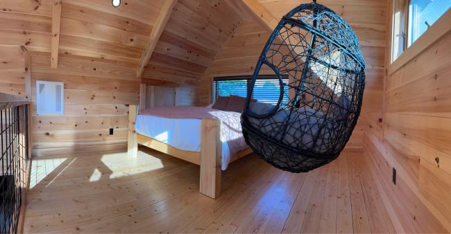 Wide angle view of loft bedroom with angled roofline and hanging egg chair.