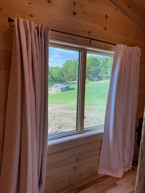 Finished framed window installation with curtains looking out upon Maine woods.