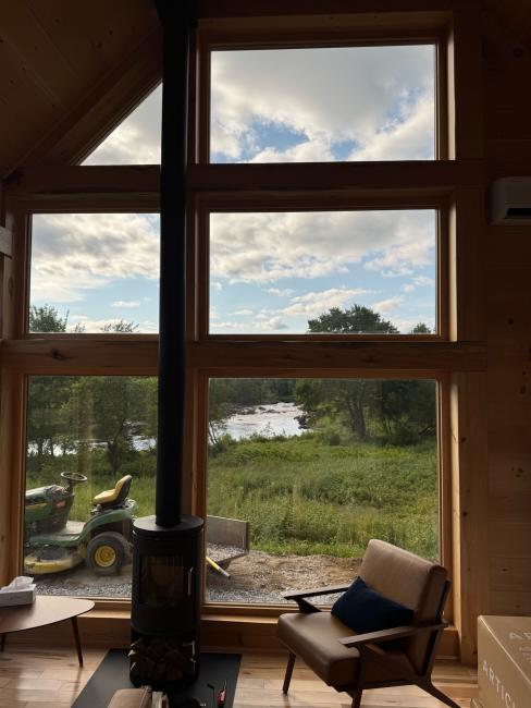 Bucolic views outside large cabin windows with a wood burning stove.