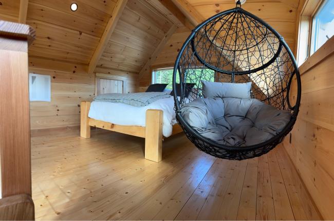 Loft sleeping area with wood vaulted ceilings and hanging basket egg chair installed.