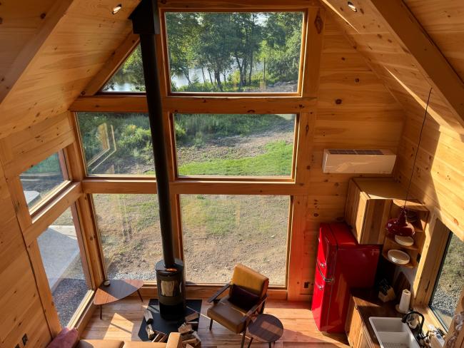 View of the large windows that open into the living room and kitchen of this cabin getaway in Maine.