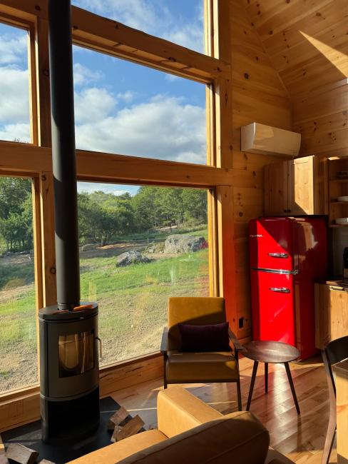 View of surrounding Maine landscape through large, wall-height windows and cozy fireplace.