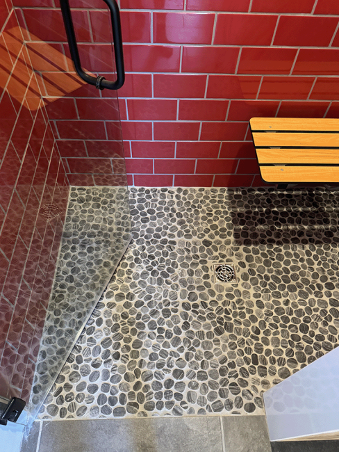 Finished walkin ADA shower with red tile, seating that folds down, and natural smooth stone floors.