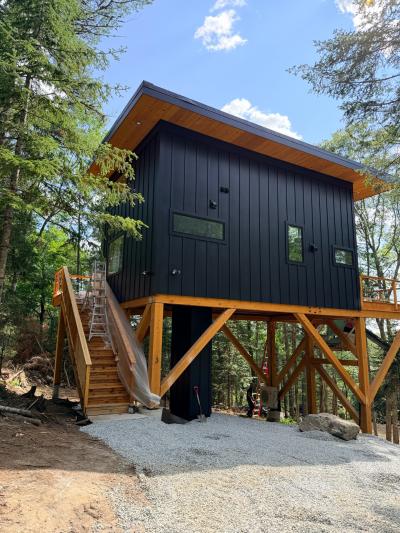 Cabin on stilts with dark siding and gravel driveway.