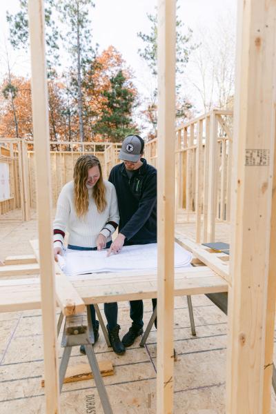 Couple standing at an unfinished construction project looking at architectural drawings.